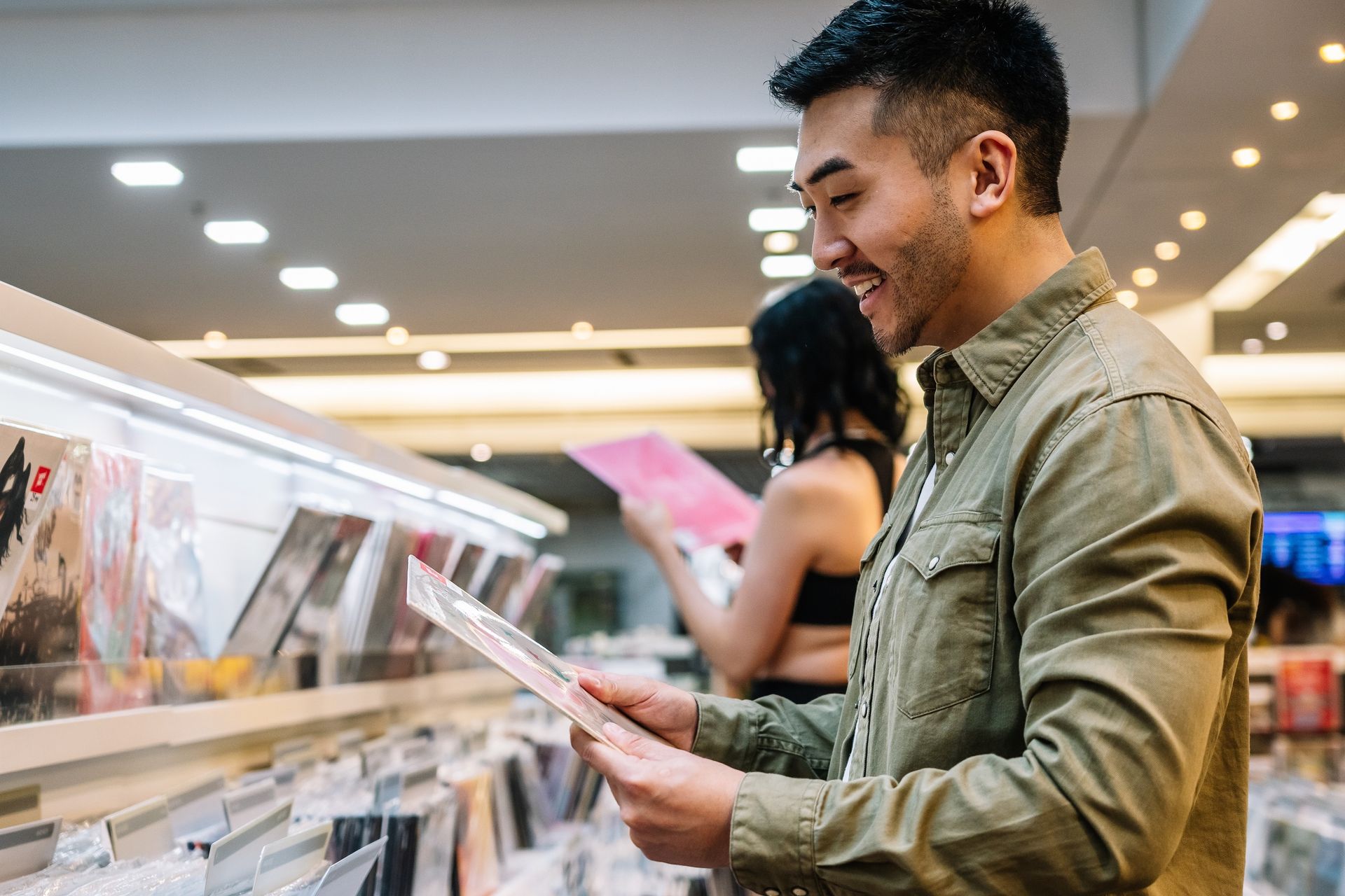 Man browsing records in a music store, smiling while flipping through albums in a brightly lit aisle