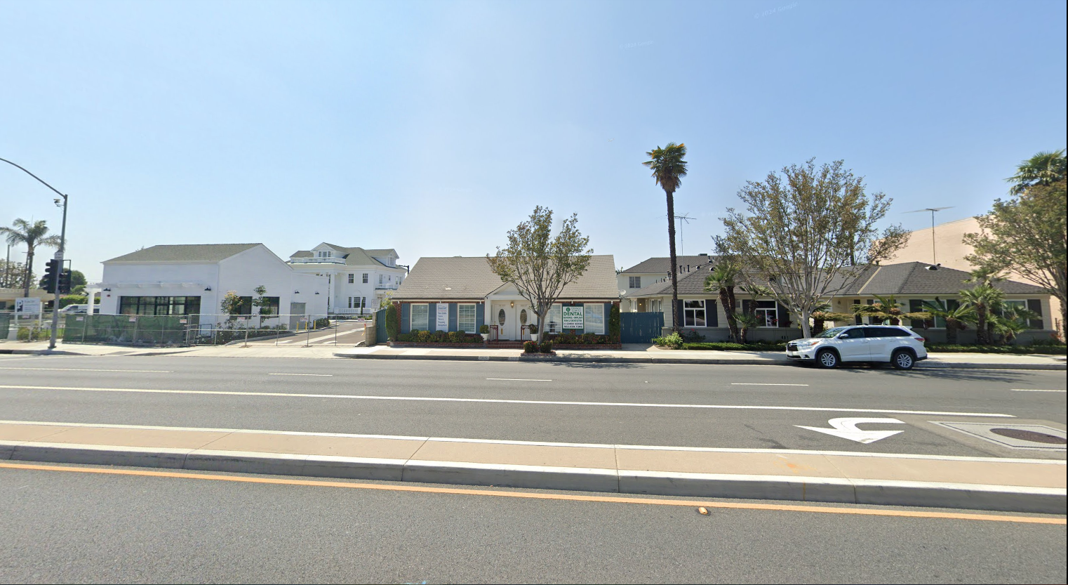 A white suv is parked on the side of the road in front of a row of houses.