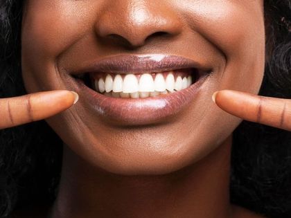 A woman is smiling and holding her fingers to her mouth.