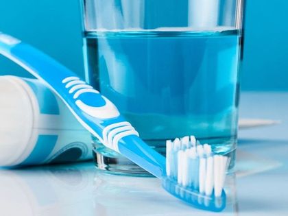 A toothbrush , toothpaste , mouthwash and a glass of water on a table.