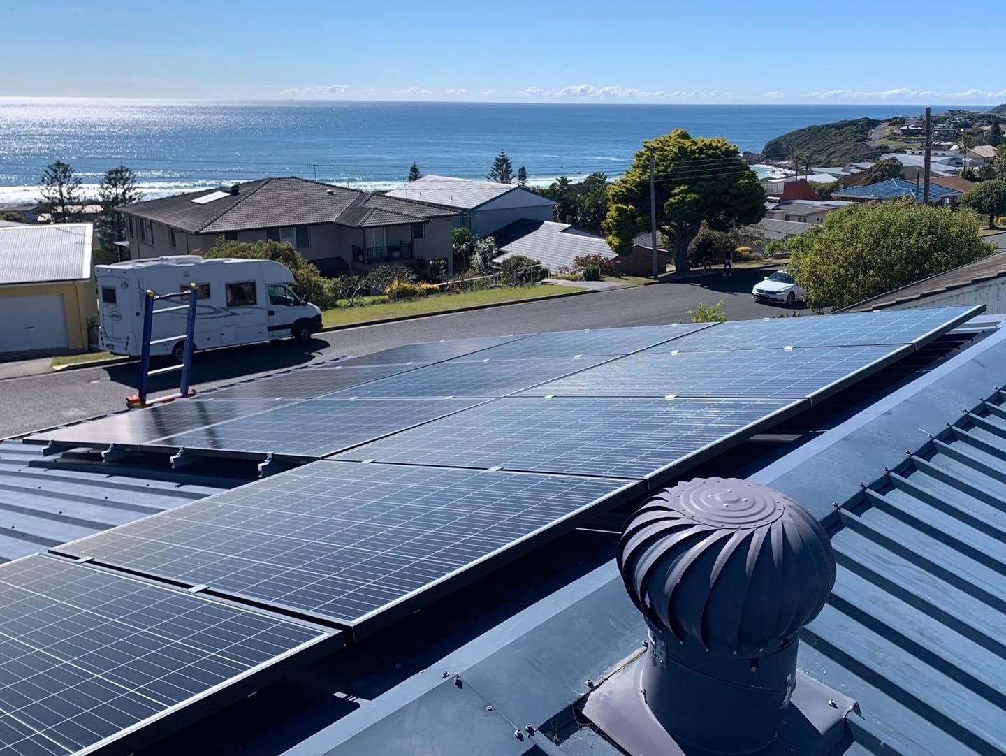 Solar Panels on a Roof Overlooking the Ocean, With Houses and a Van in the Background on a Sunny Day — Forster Solar and Lighting In Forster, NSW