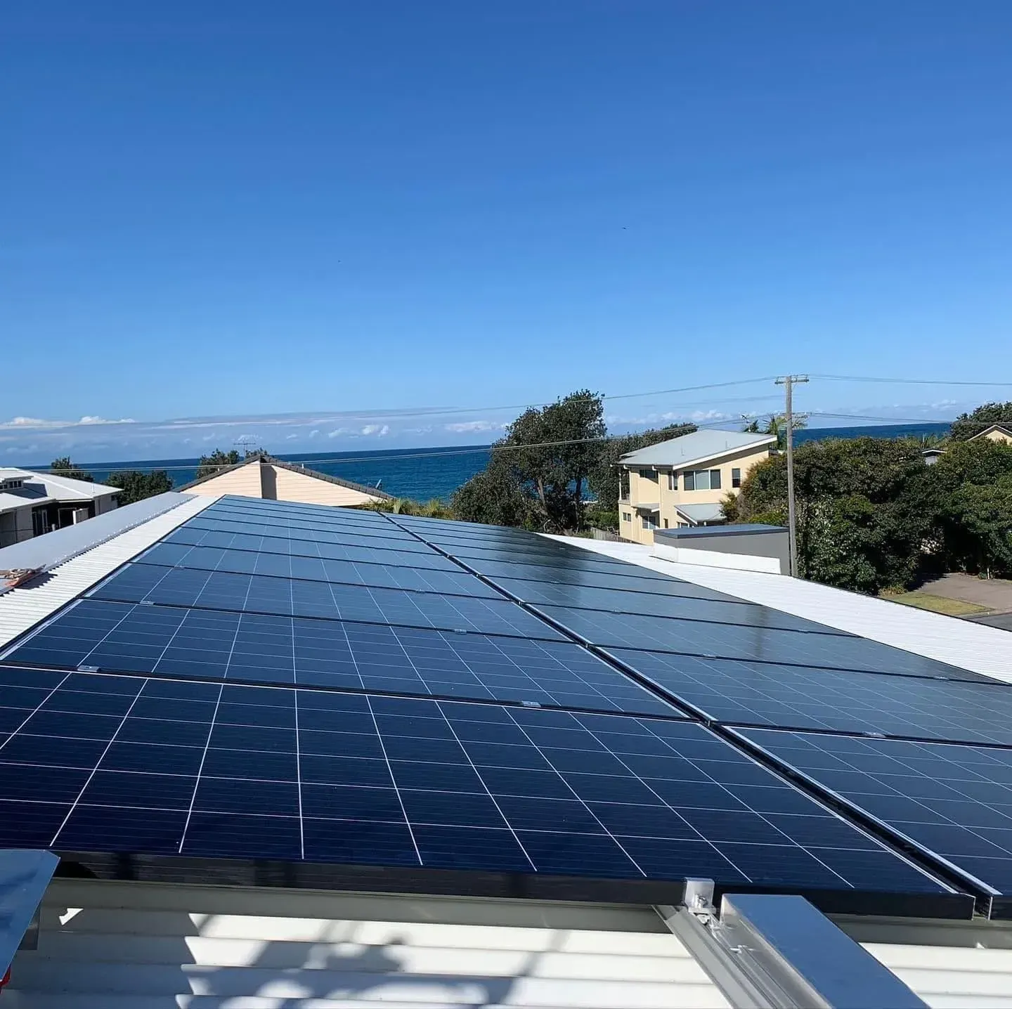 Solar Panels Installed on a Rooftop Overlooking the Ocean Under a Clear Blue Sky — Forster Solar and Lighting In Forster, NSW