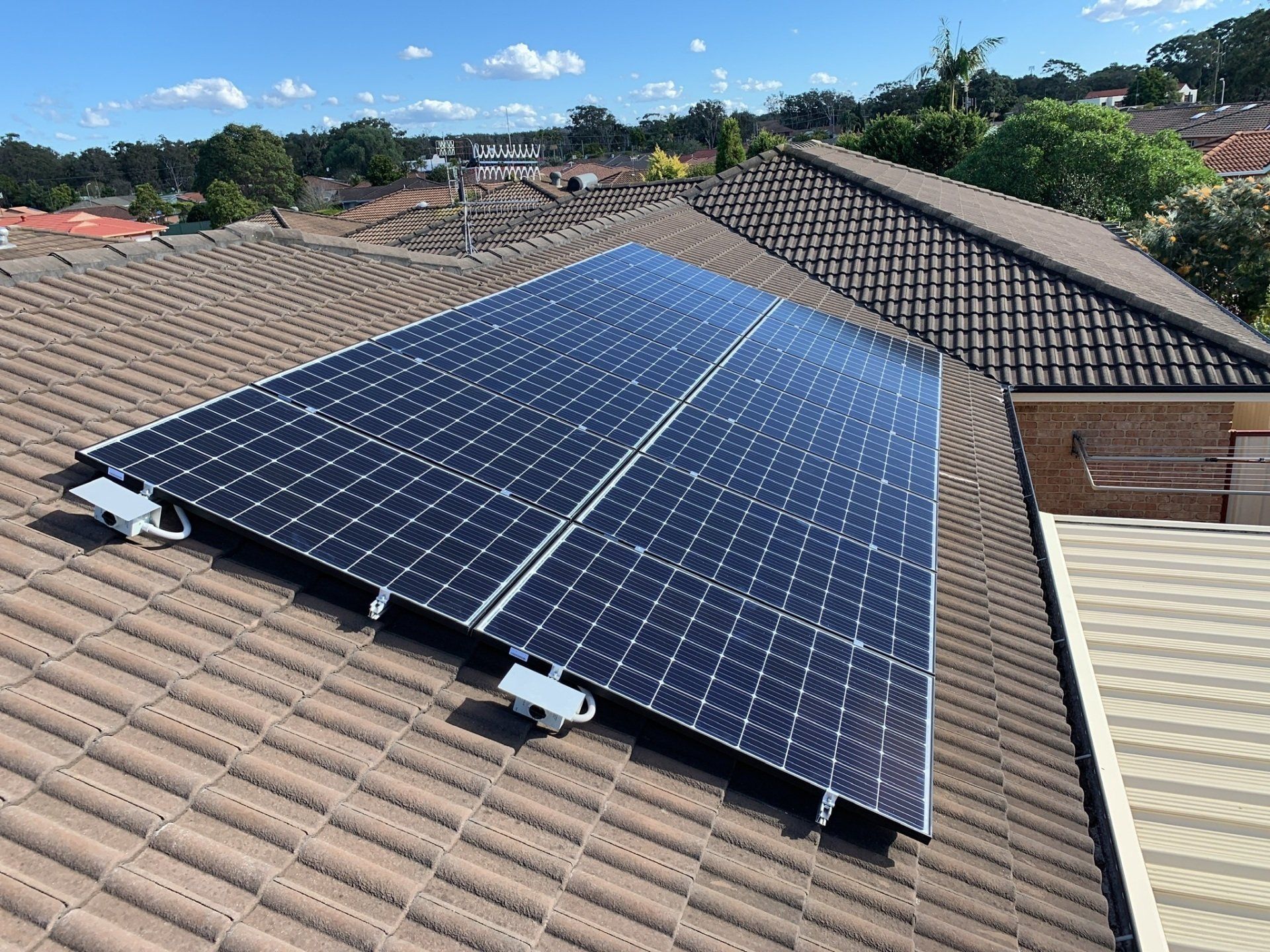 Solar Panels Installed on a Brown Tile Roof With Blue Sky in the Background — Forster Solar and Lighting In Forster, NSW