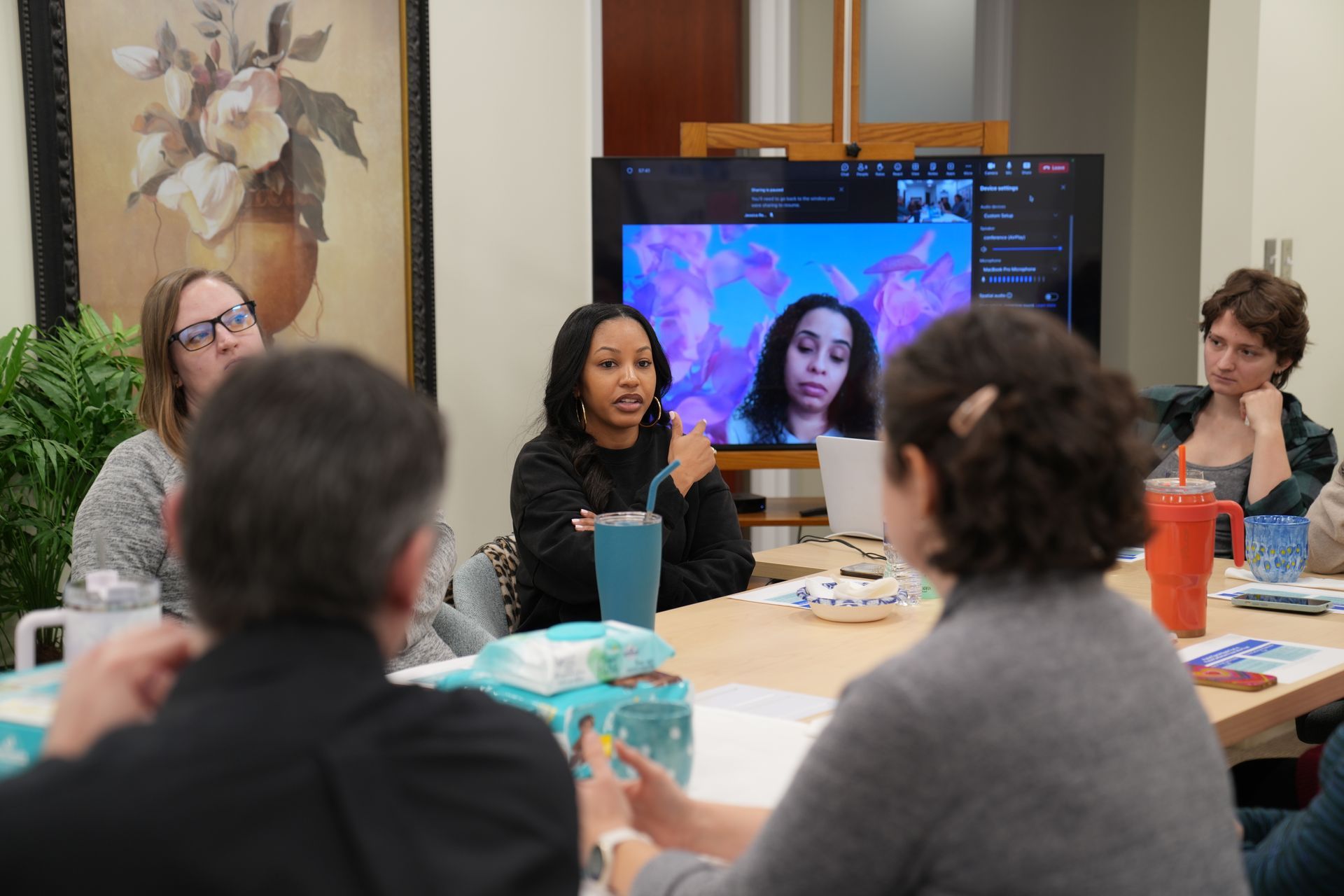 Special Needs: A group of people are sitting around a table in front of a television.