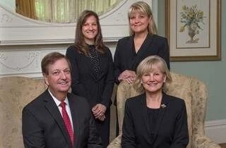 Four people posing for a photo in a room with a decorative mirror and painting.