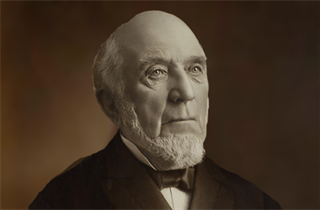 Portrait of an older man with white hair, beard, and serious expression; wearing a dark suit and bow tie.