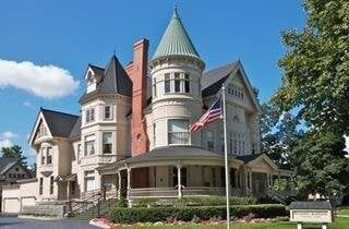 Large, ornate beige building with a green-topped tower, American flag, and surrounding greenery under a blue sky.
