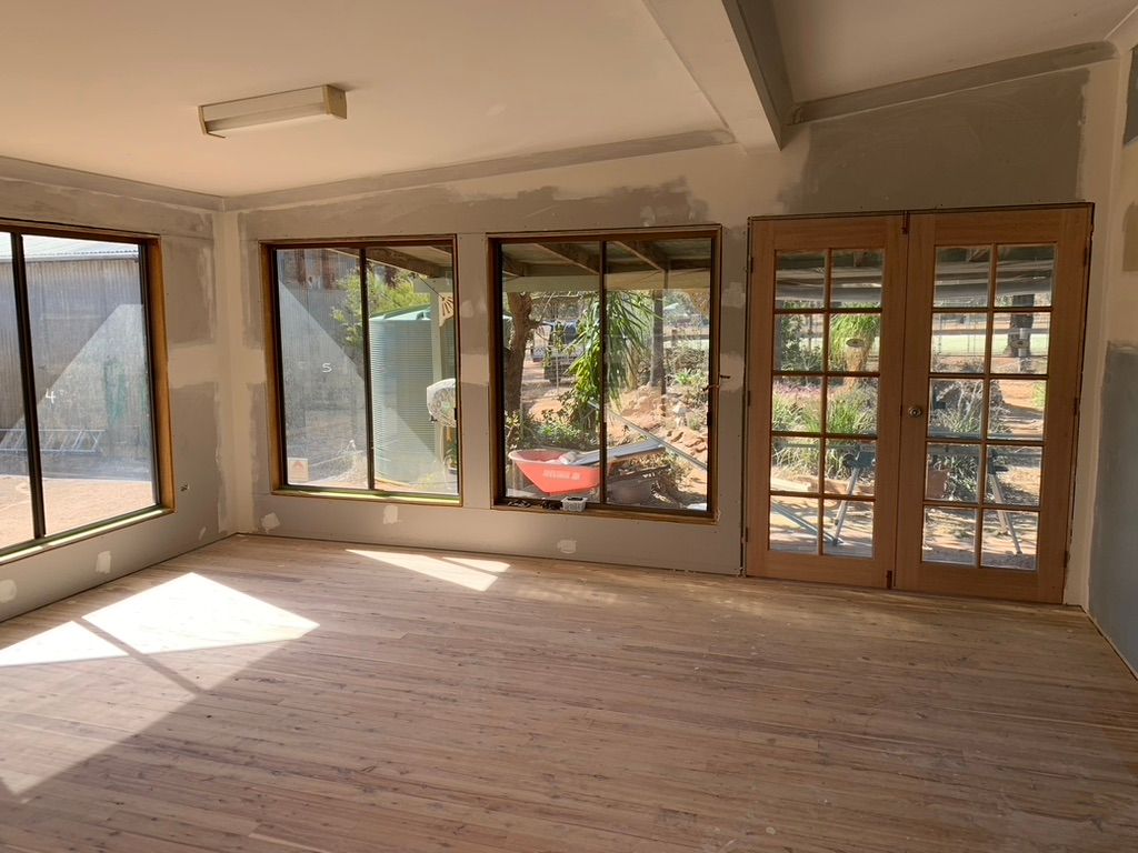 Wooden deck with white railing next to a house with a glass door. Green garden hose hangs on the wall.