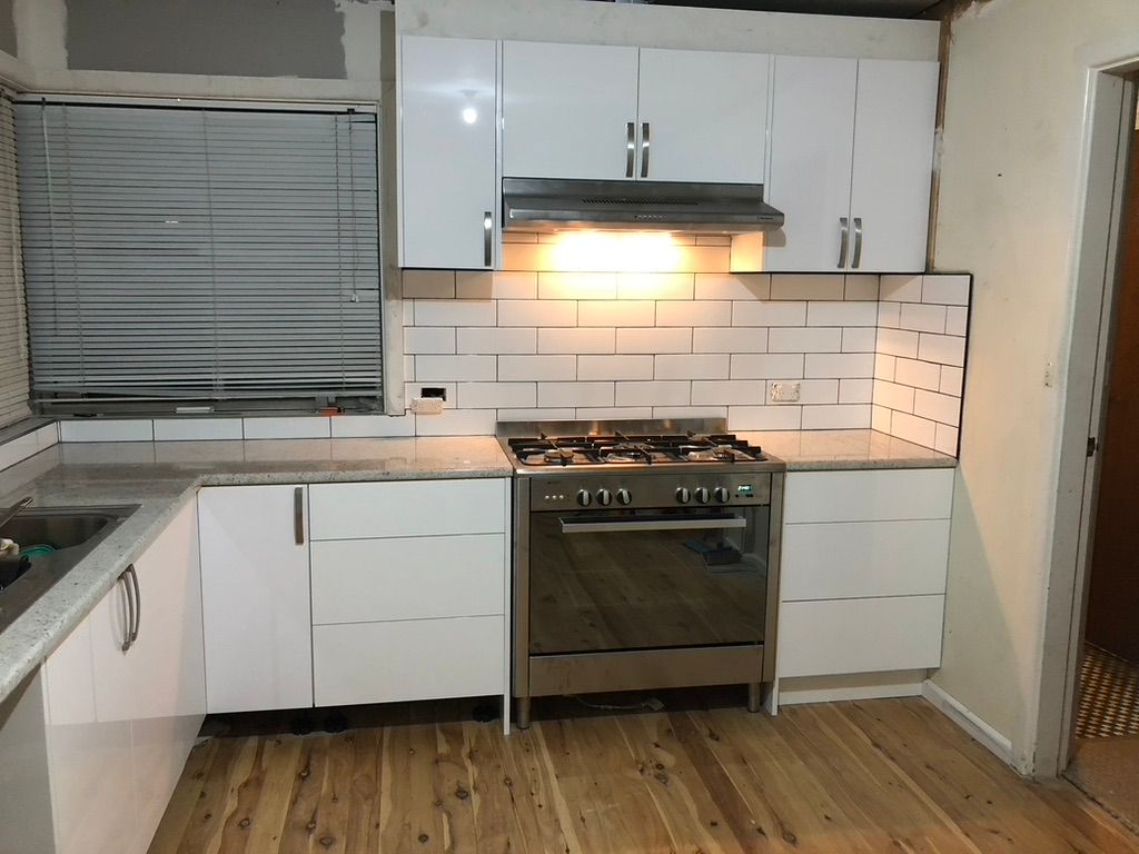 Kitchen renovation in progress: white cabinets installed, island base in the foreground, hardwood floors, and a small window.