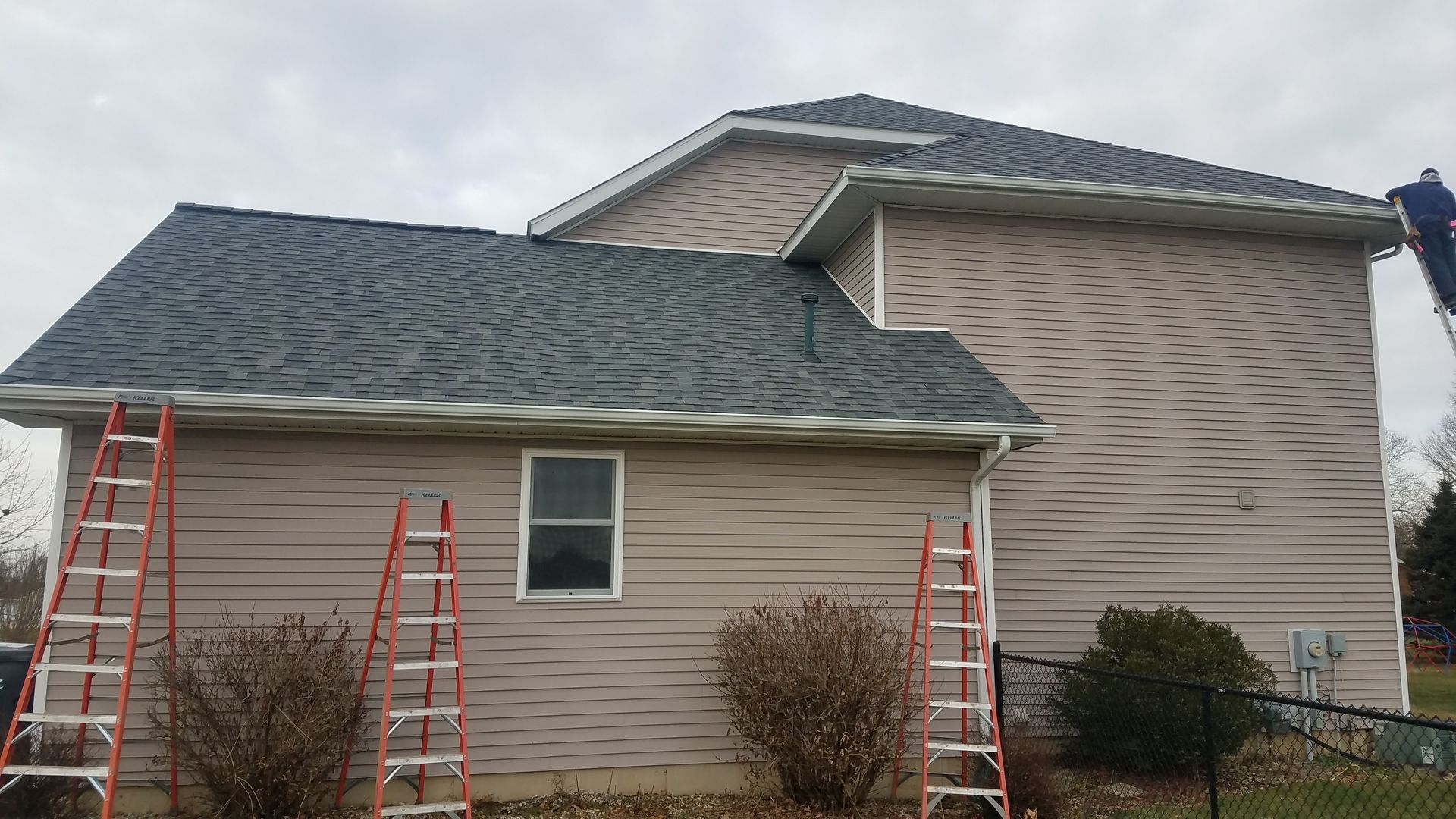 A man on a ladder is working on the roof of a house.