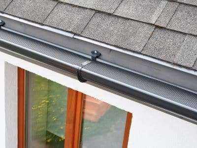A close up of a gutter on a roof next to a window.