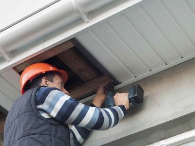 A man wearing a hard hat is working on the ceiling of a building.