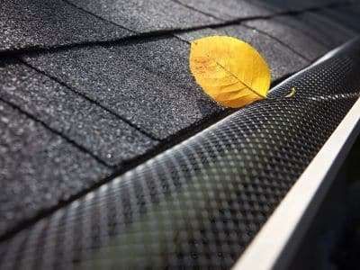A yellow leaf is sitting on top of a gutter on a roof.