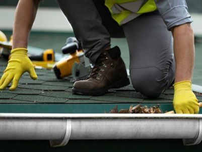 A man wearing yellow gloves is working on a roof.