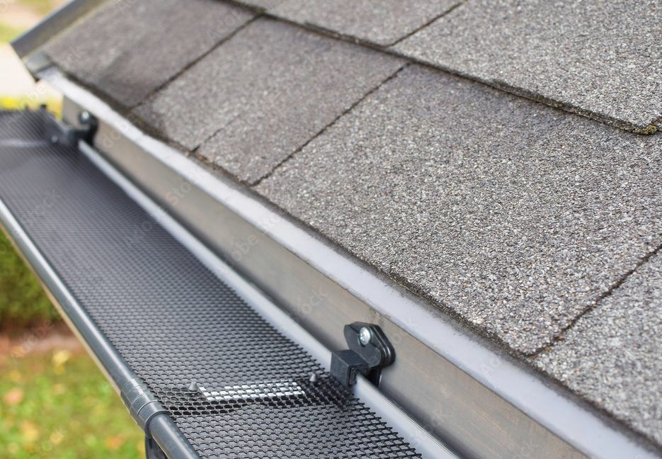 A close up of a gutter on a roof with shingles.