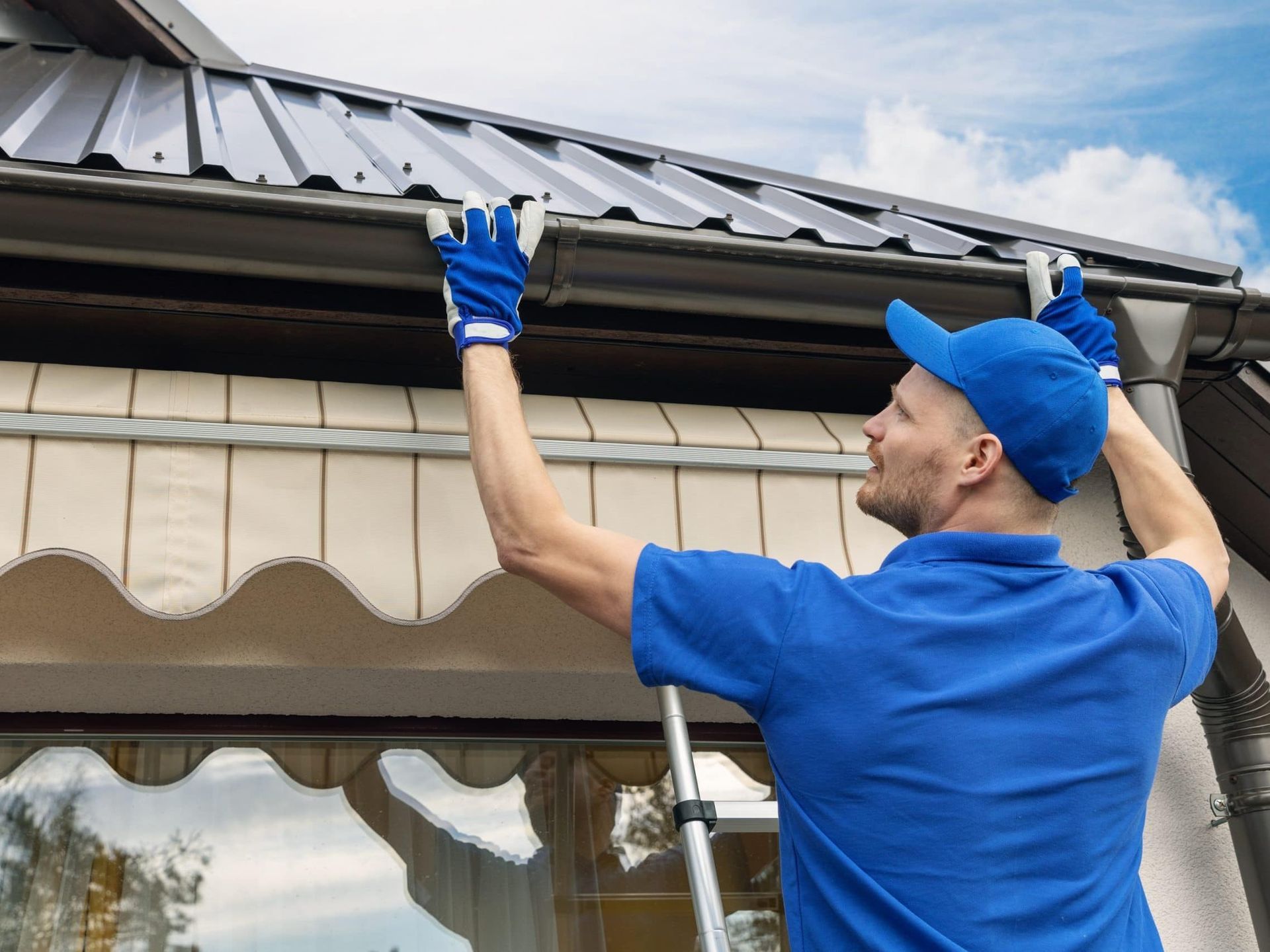 A man is standing on a ladder fixing a gutter on a roof.