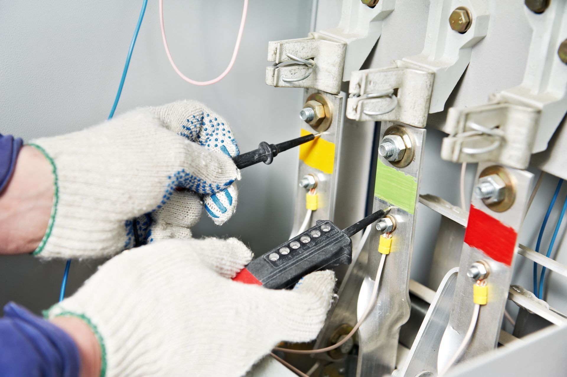 Mani con guanti da lavoro usano un tester di tensione sulle barre metalliche di un quadro elettrico.