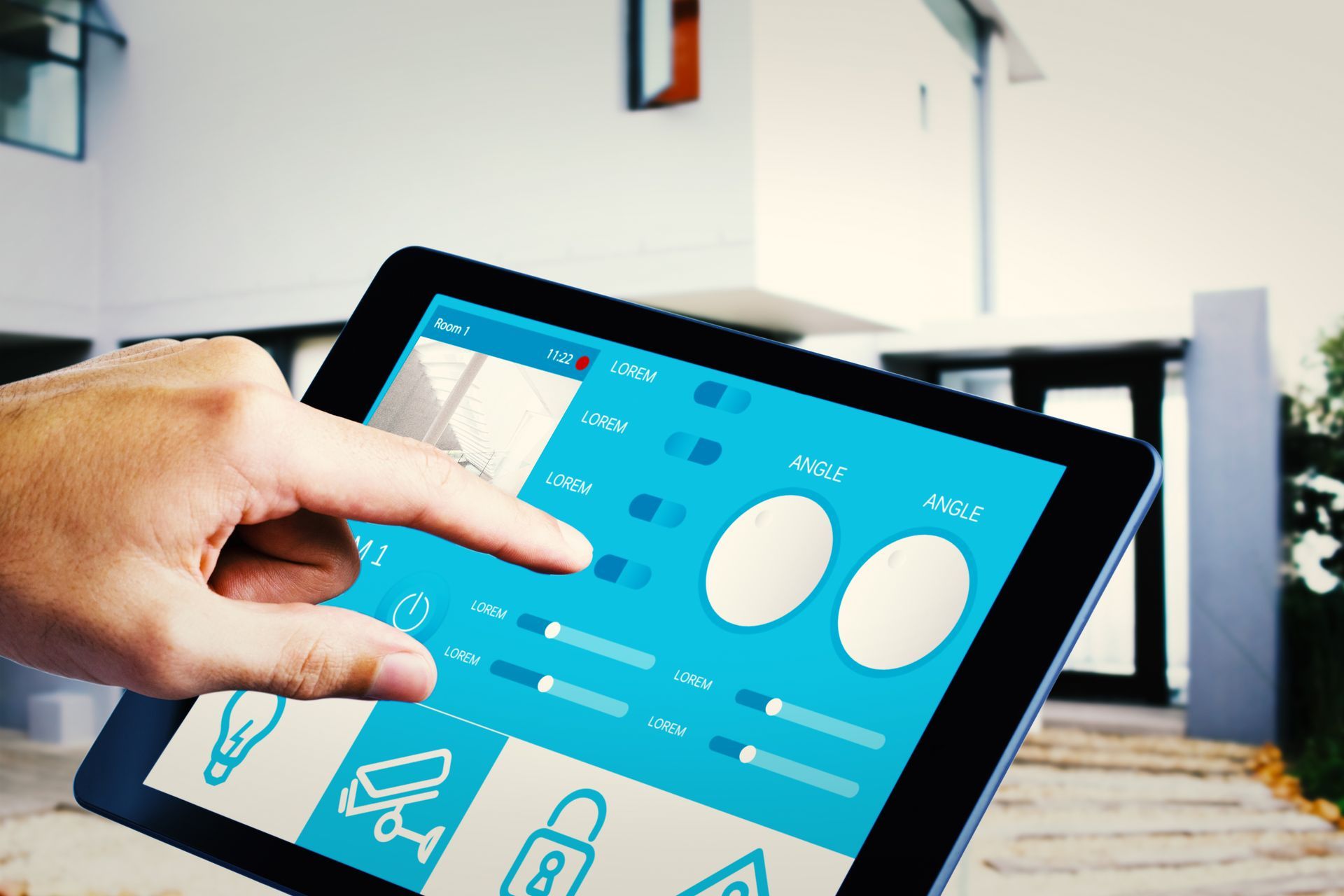 Una mano tocca lo schermo di un tablet che mostra un'interfaccia blu per il controllo della domotica, davanti a una casa moderna.