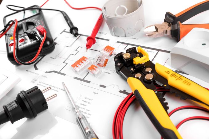 Attrezzi elettrici, connettori per cavi, un multimetro e schemi elettrici sparsi su una superficie bianca.
