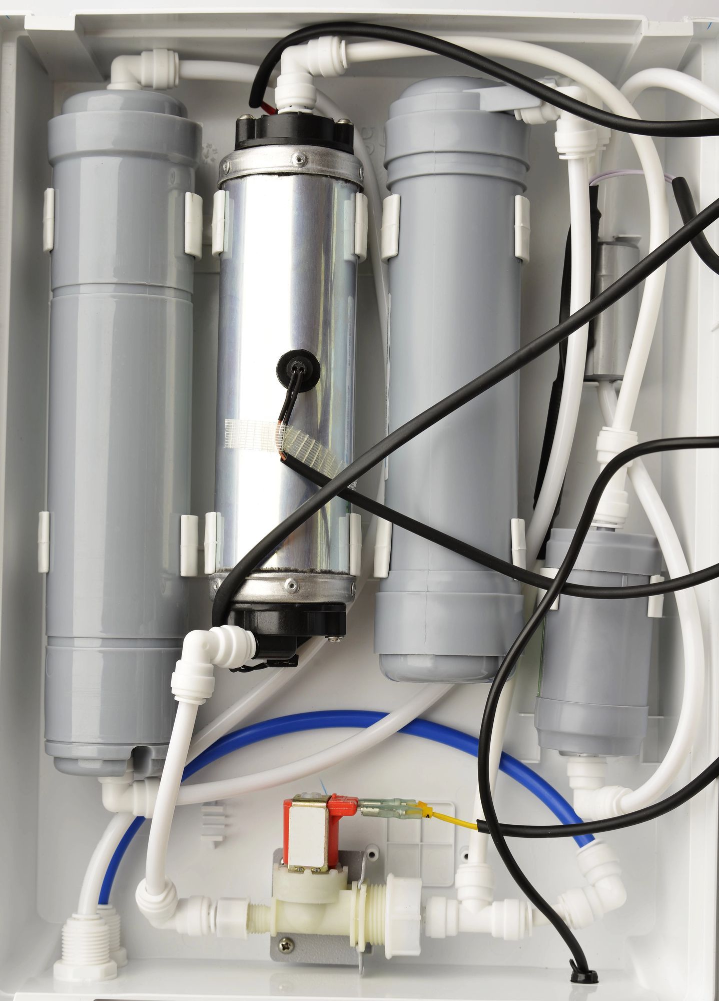 Vista interna di un'unità di filtrazione dell'acqua con tre contenitori filtranti verticali, tubi e una piccola valvola solenoide.