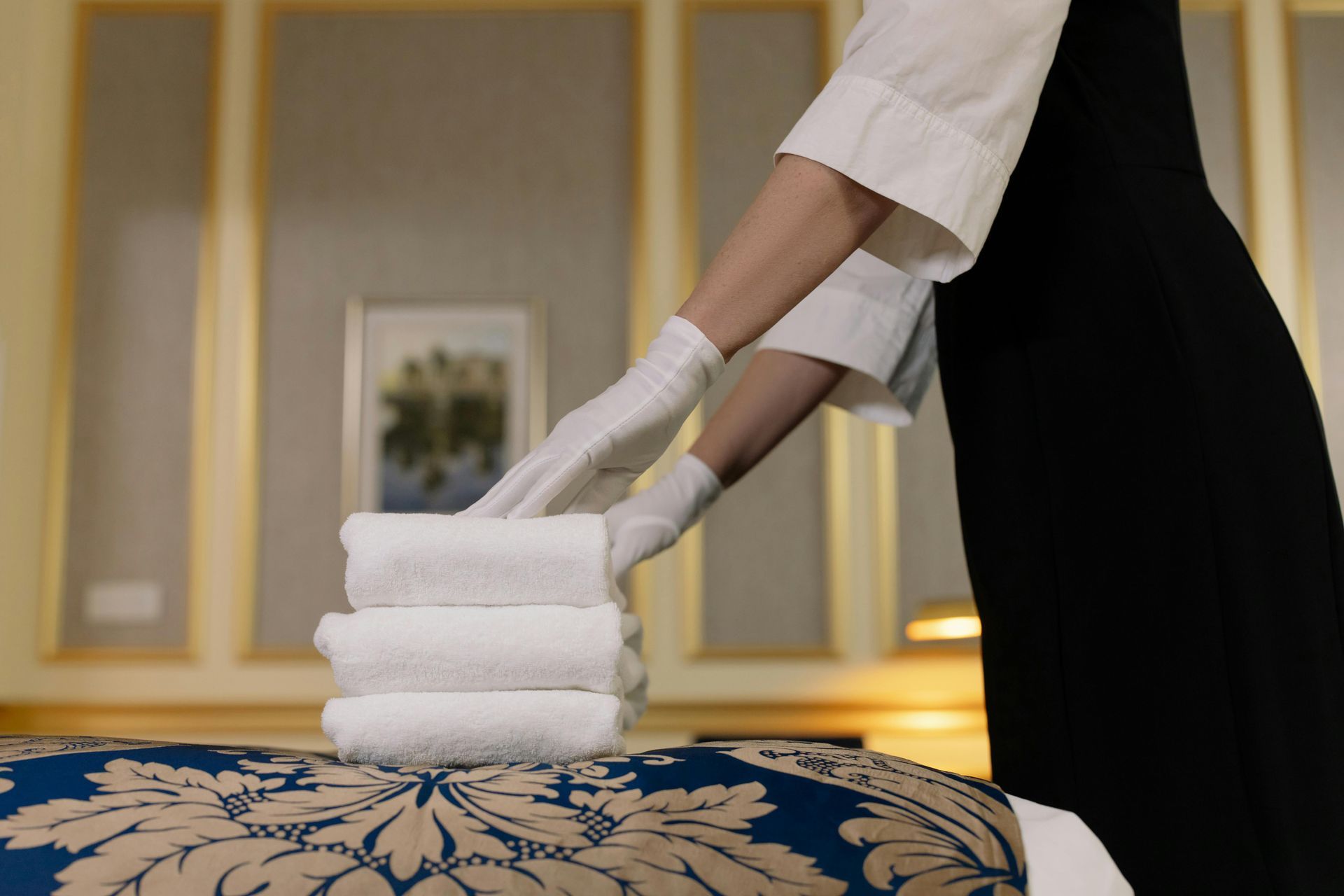 A maid is stacking towels on a bed in a hotel room