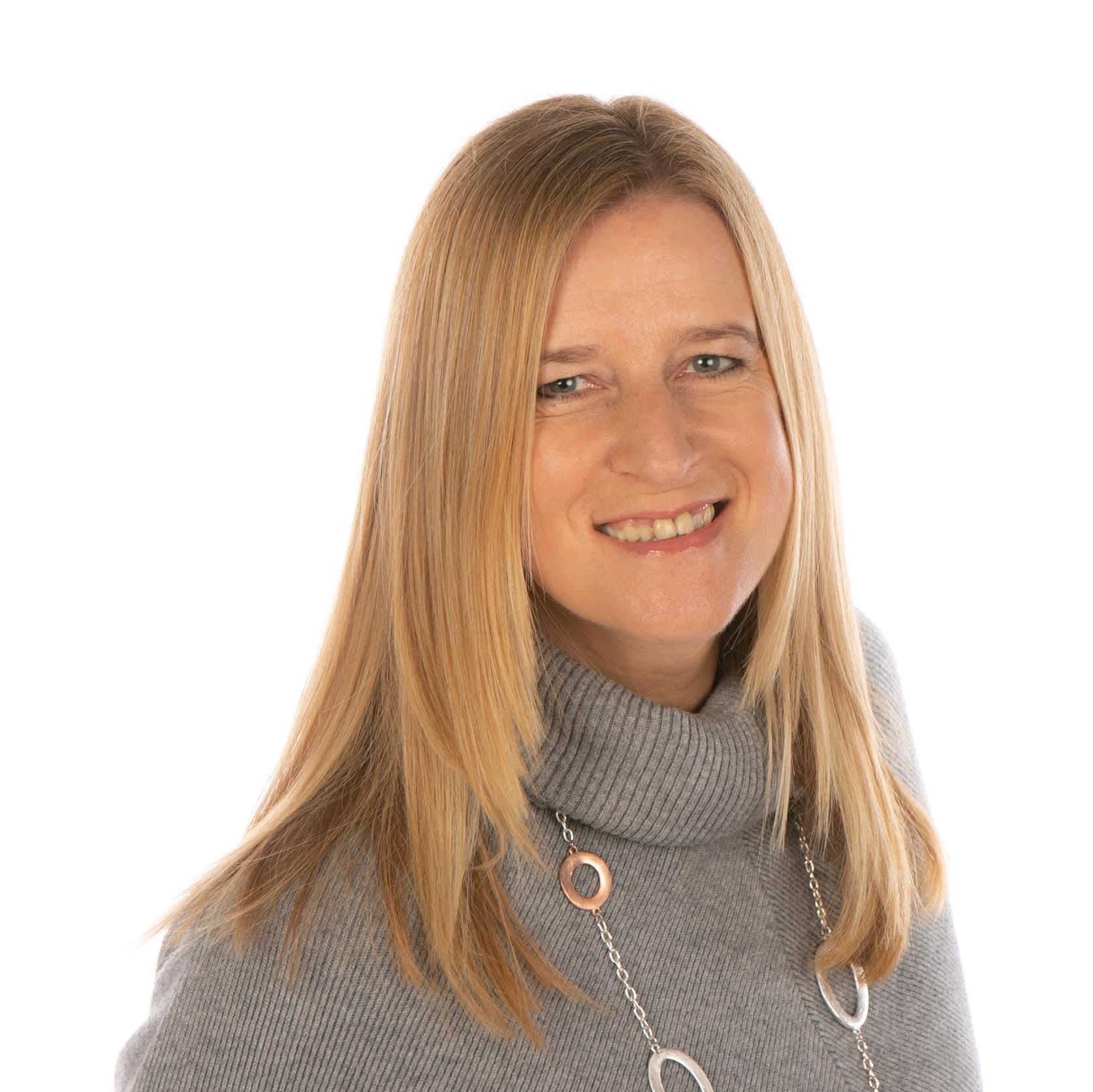 a woman in a grey sweater and necklace is smiling for the camera .