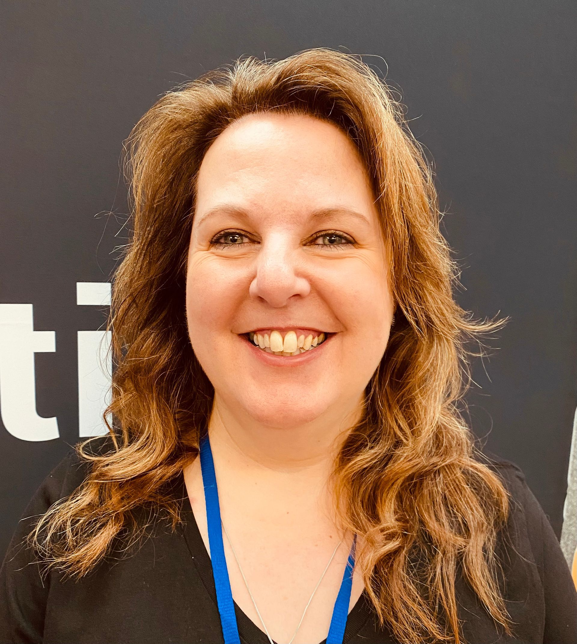 A woman wearing a black shirt and a blue lanyard is smiling.