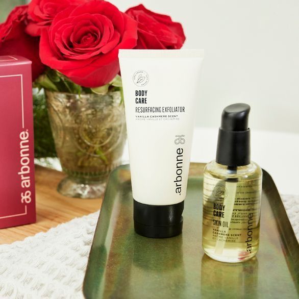 A bottle of arbonne lotion sits on a tray next to a vase of red roses