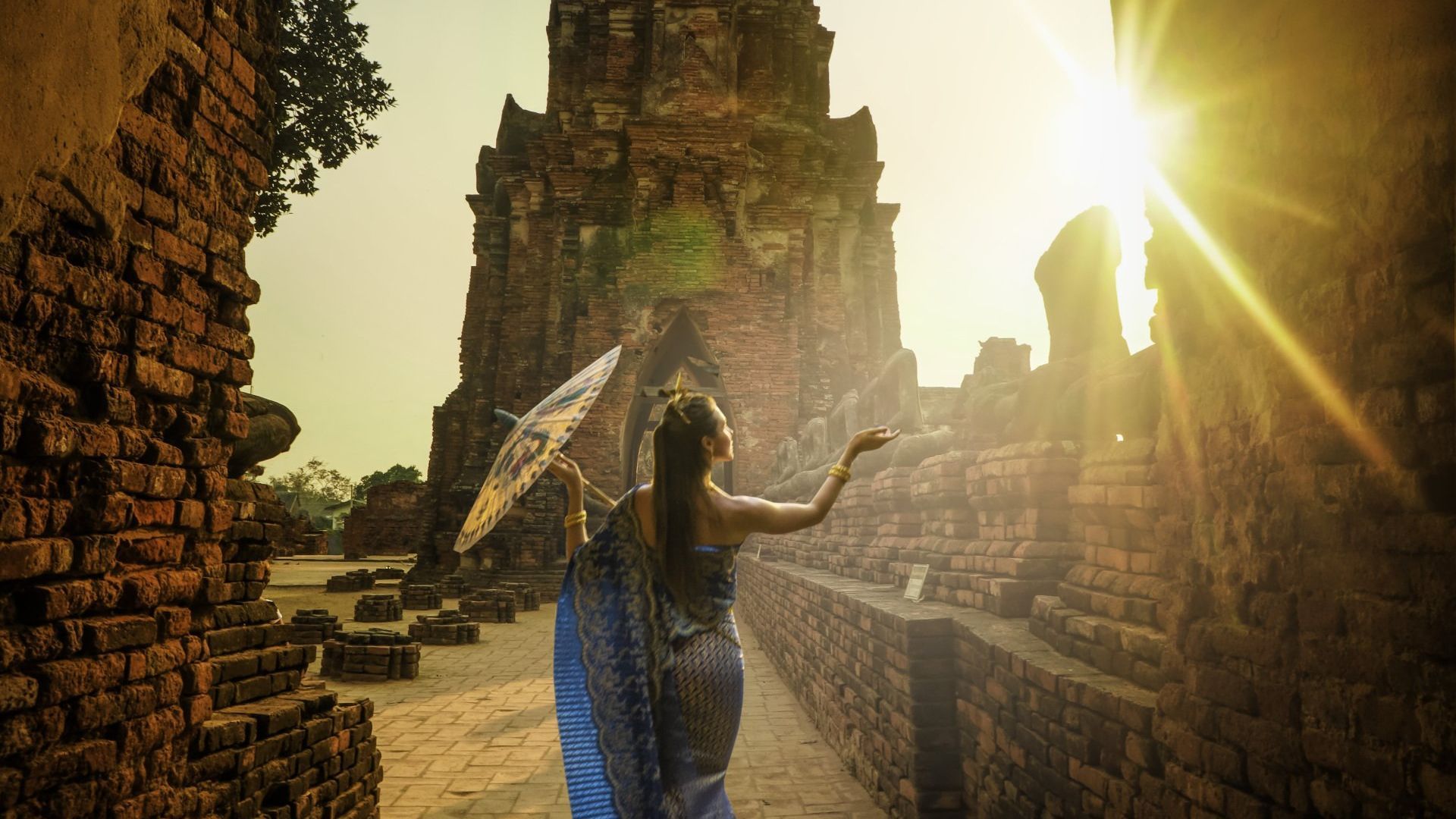 A woman is holding an umbrella and walking in front of a brick wall.