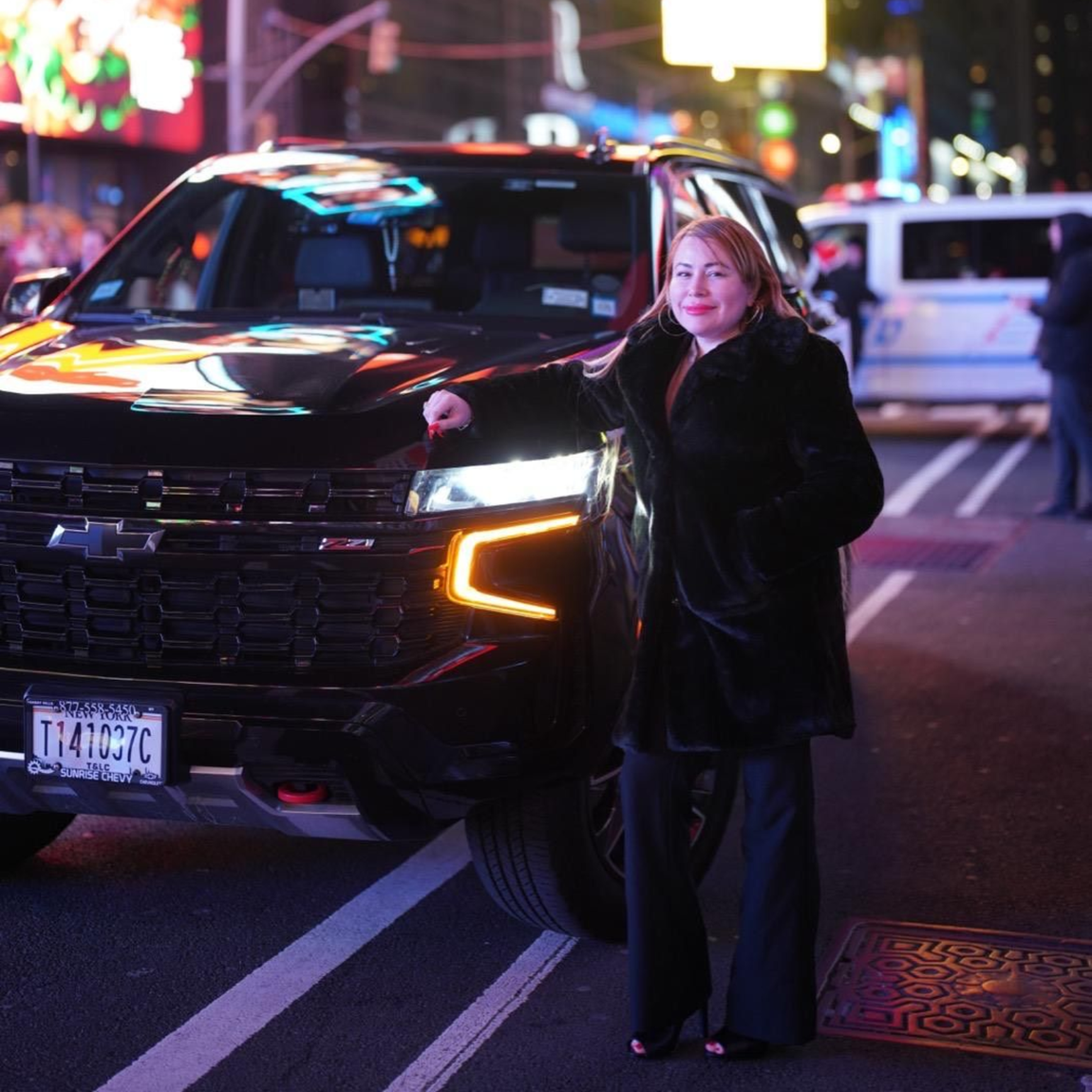 Dark Mercedes-Benz sedan parked at night with city skyline in the background. Headlights on.