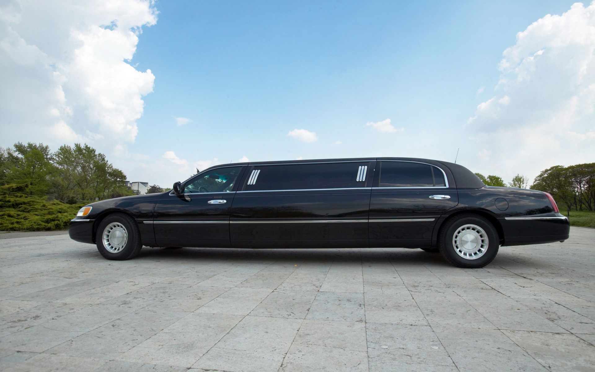 Black limousine parked on a concrete surface against a blue sky with clouds.