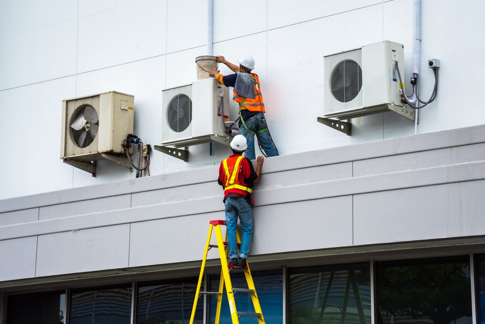 Two aircon technician cleaning aircon outside a building