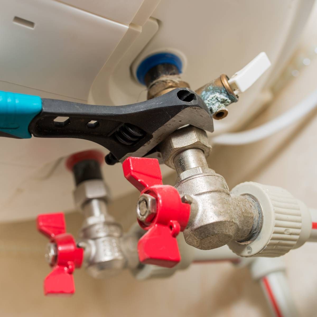 Wrench tightening a valve on a water heater, with red-handled shut-off valves and white pipe connections.
