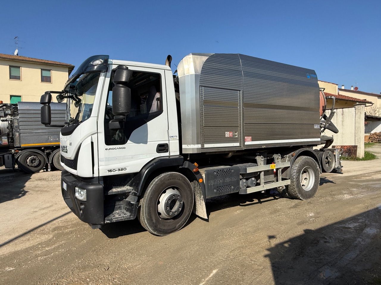 Primo piano di un'autocisterna blu per lo scarico delle fosse settiche con un tubo verde collegato alla valvola di un serbatoio.
