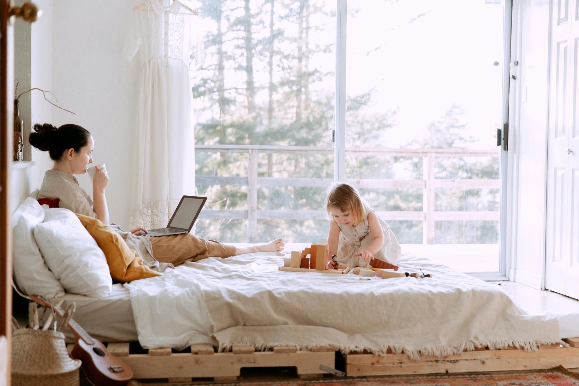 image of a mom and baby on a bed while mom is on the computer