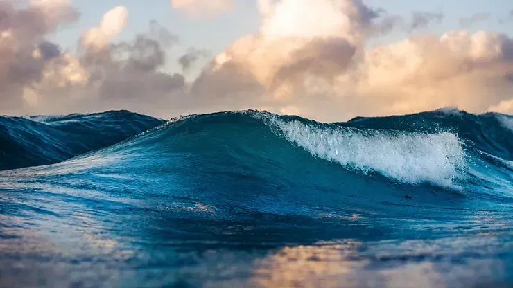 Una grande onda nell'oceano con un cielo nuvoloso sullo sfondo.