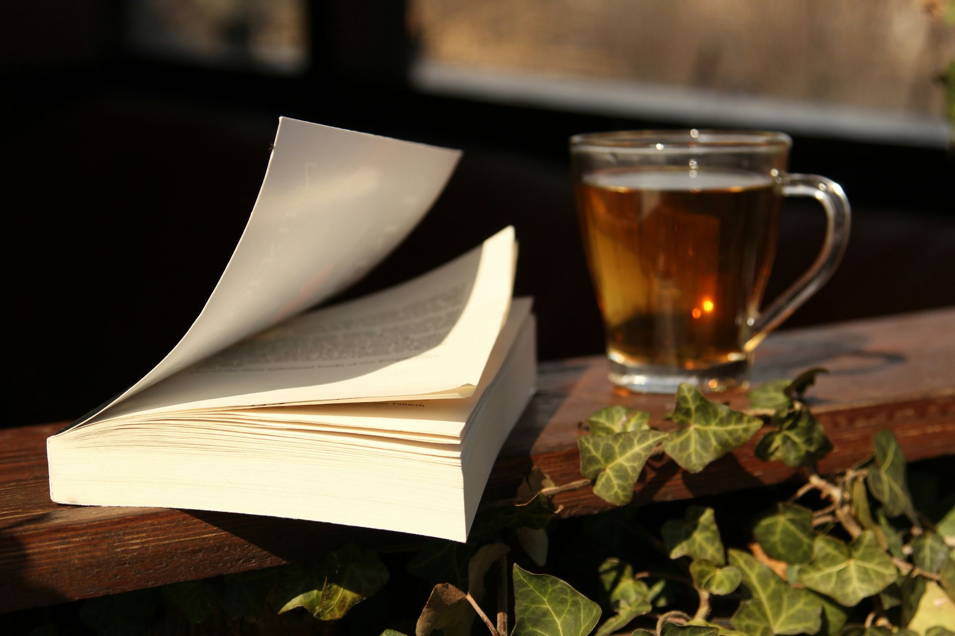 A carafe of tea sits on a wooden board next to a book.