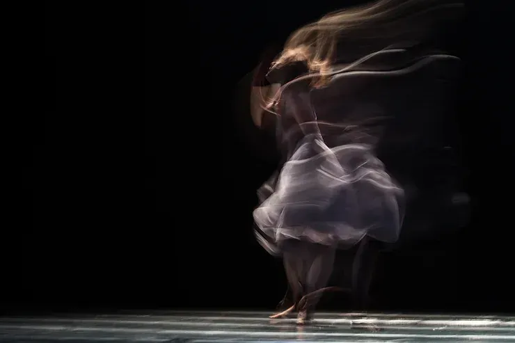 Un'immagine sfocata di una donna in abito bianco che balla su un palco.