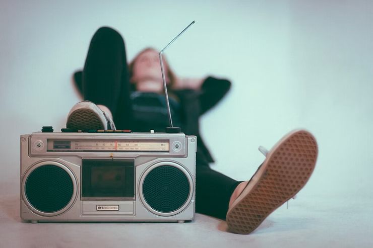 Una persona è sdraiata sul pavimento mentre ascolta musica con i piedi su uno stereo portatile.