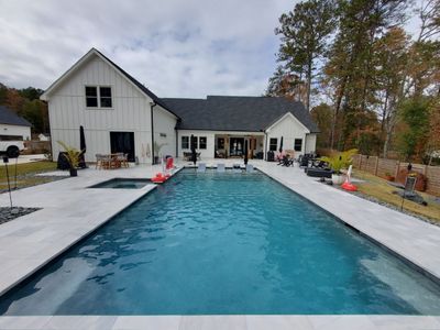Backyard swimming pool beside a white house with pool deck and patio seating