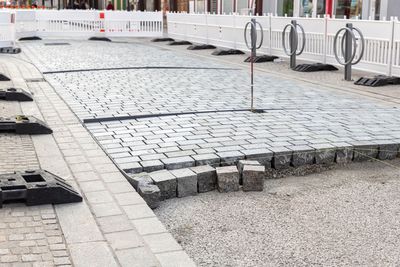 Cobblestone-paved walkway under construction with a raised edge and metal bike racks nearby