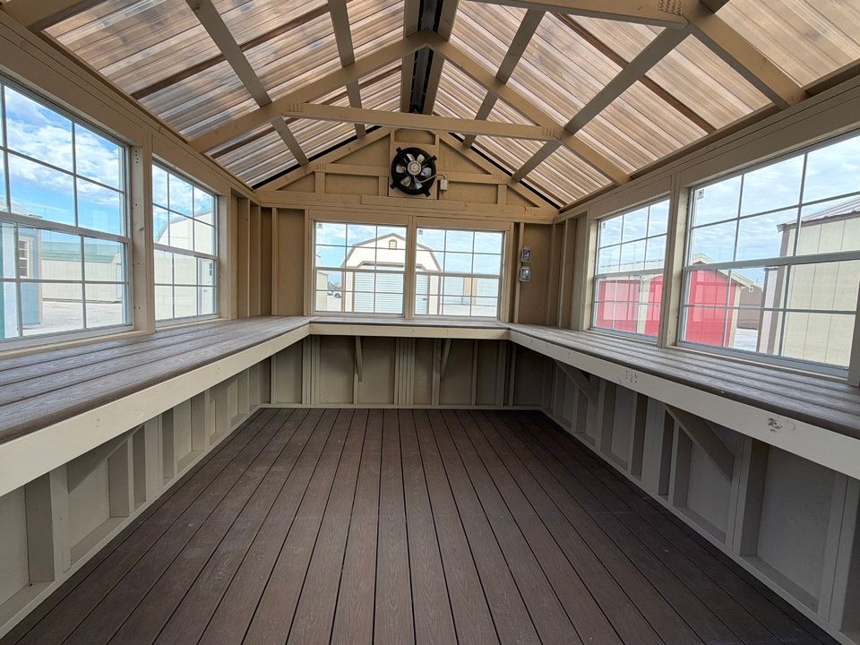 Interior of a greenhouse with windows and benches, brown floor, and clear roof panels.