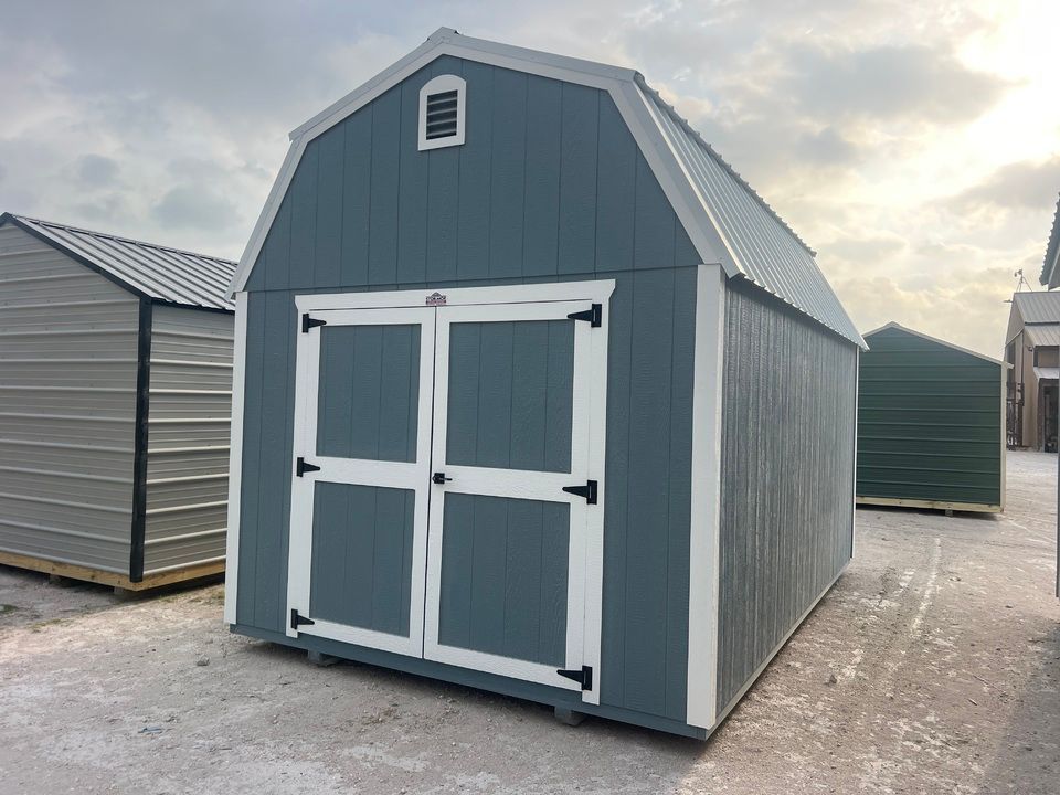 Blue and white barn-style shed with a metal roof. Other sheds are visible in the background.