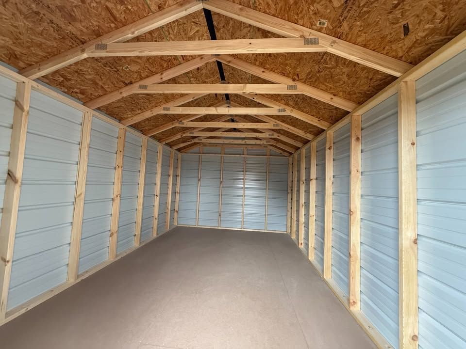 Interior view of a rectangular shed with a wooden frame and metal siding. Empty space with brown floor.