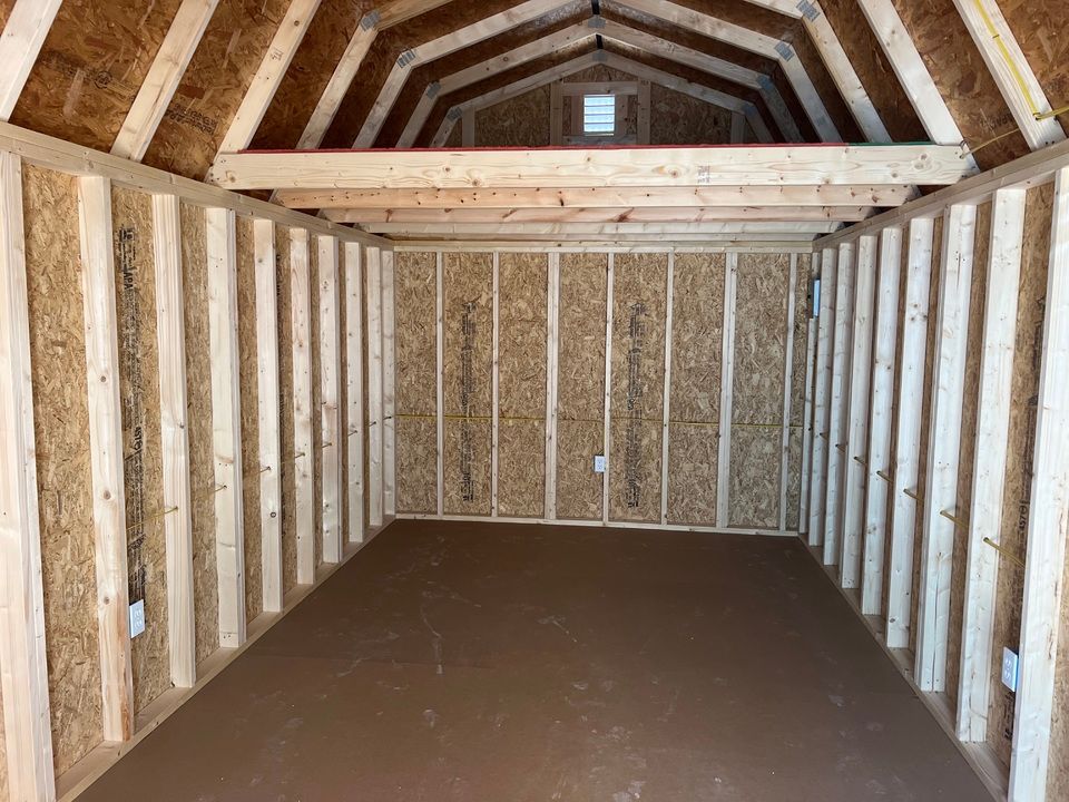Interior view of an empty wooden shed with bare wooden framing and a brown floor.