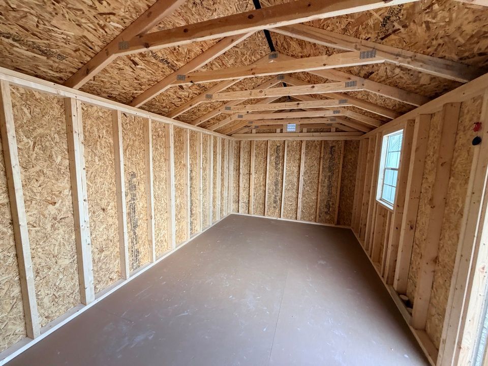 Interior view of a wooden shed with plywood walls, sloped ceiling, and a window.