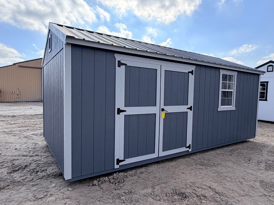 Gray shed with white trim, metal roof, double doors, and a small window.