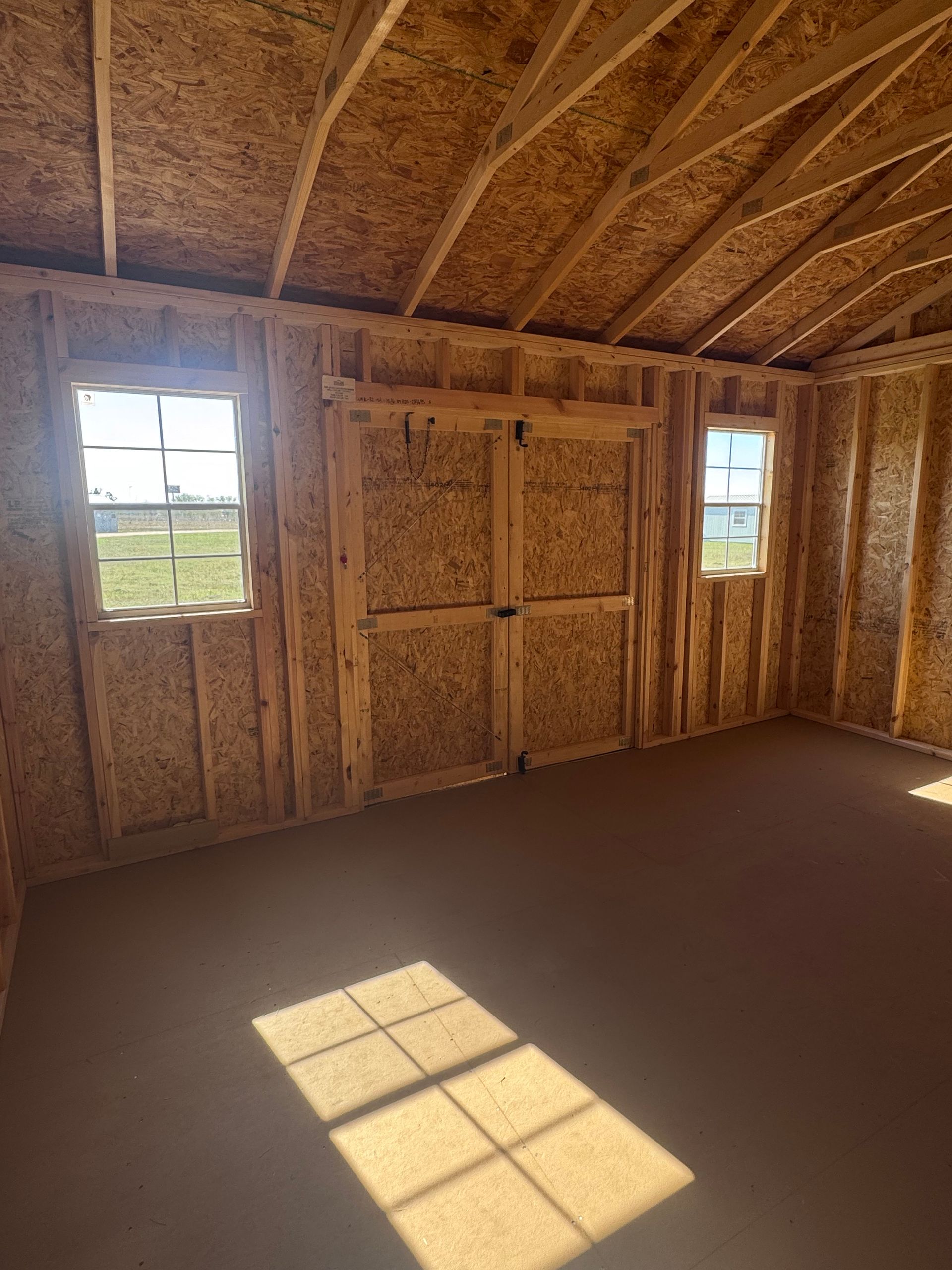 Interior of a new shed with light brown walls and roof. Two windows and a double door are visible.