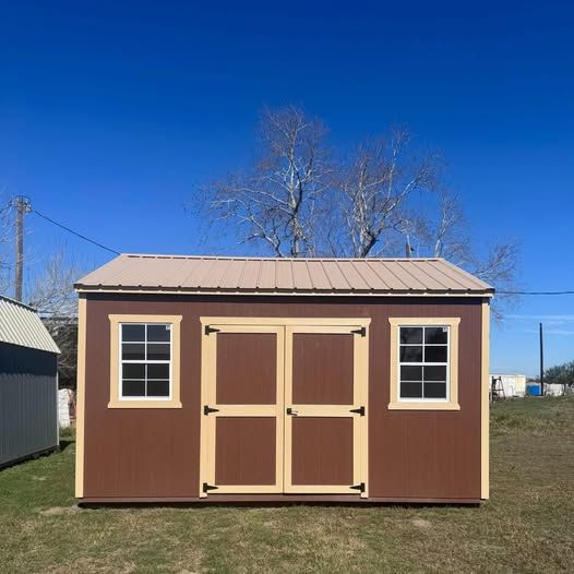 Brown and tan shed with a tan metal roof, two windows, and double doors against a blue sky.