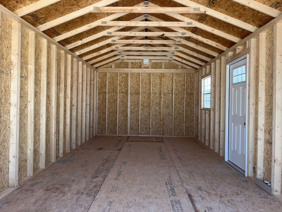 Interior view of an unfinished shed with wood frame, floor, and roof. Door and window are visible.
